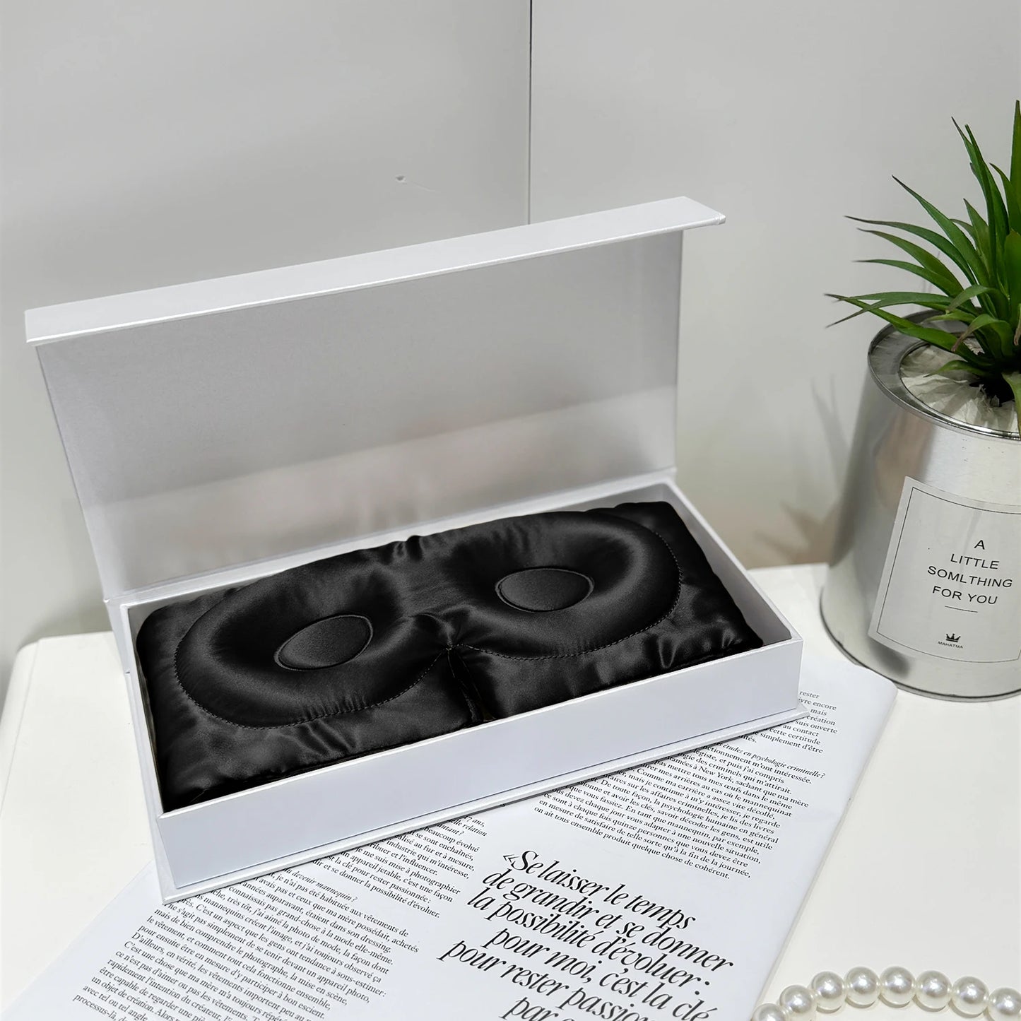 Masque de sommeil en soie noire, délicat, présenté dans une boîte blanche sur une table moderne avec des accessoires élégants
