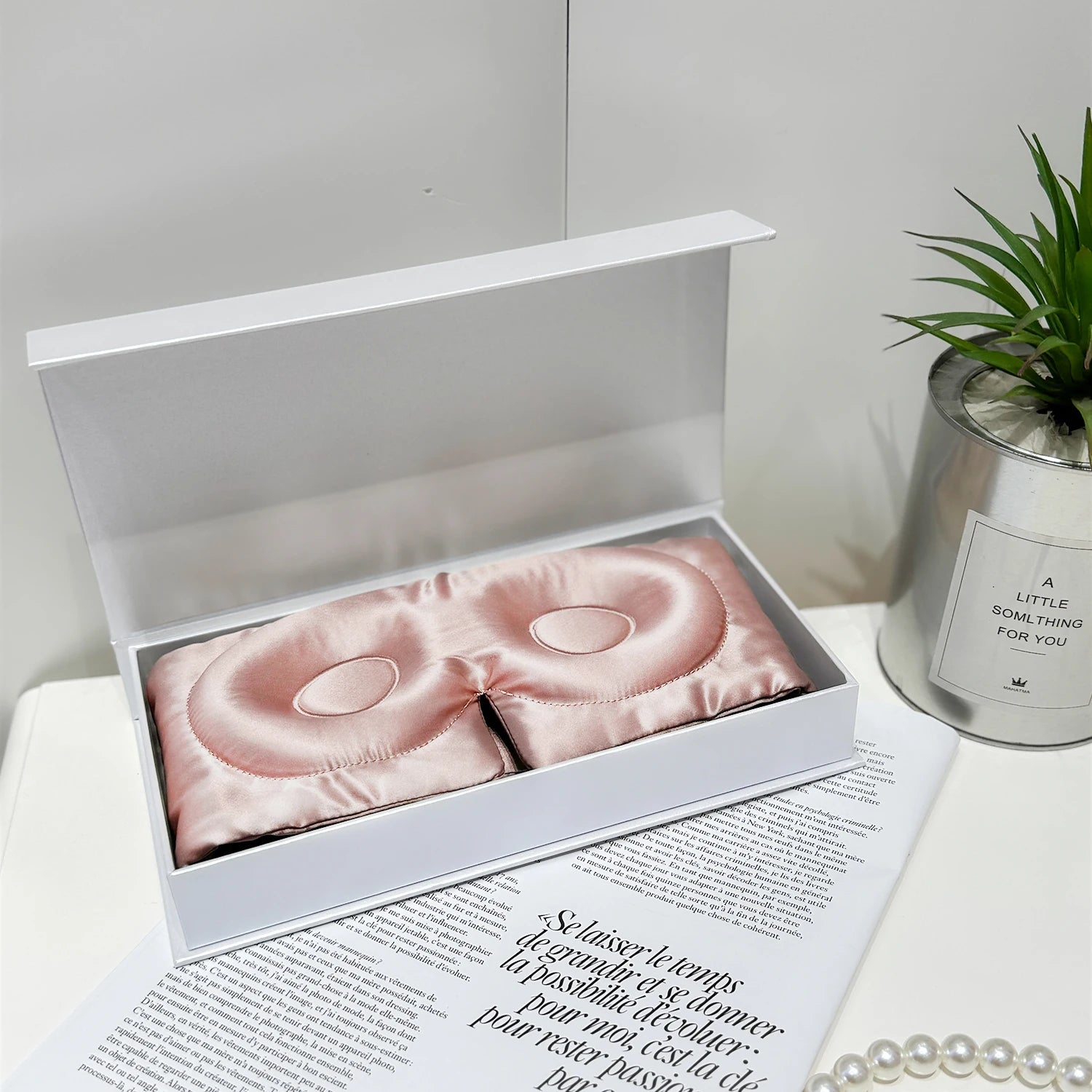 Masque de sommeil en soie rose gold, délicat, présenté dans une boîte blanche sur une surface élégante