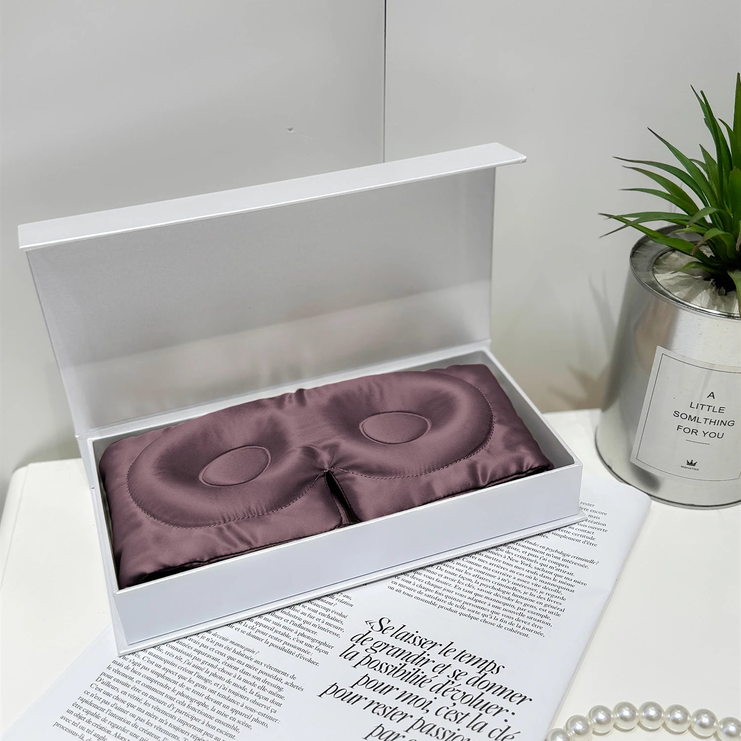 Masque de sommeil en soie mauve grise, délicatement posé dans une boîte blanche sur un fond neutre