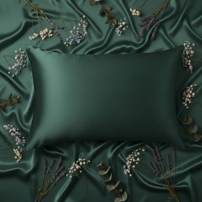 Taie d'oreiller en soie émeraude posée sur un tissu satiné avec des fleurs et des feuilles autour