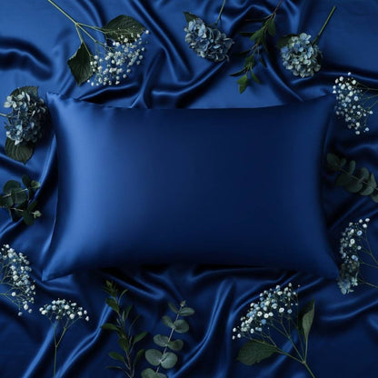Taie d'oreiller en soie bleu marine posée sur un tissu satiné avec des fleurs et des feuilles