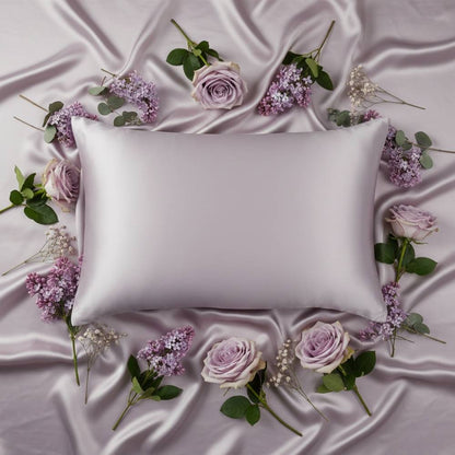 Taie d'oreiller en soie lilas entourée de fleurs roses et blanches sur un drap satiné