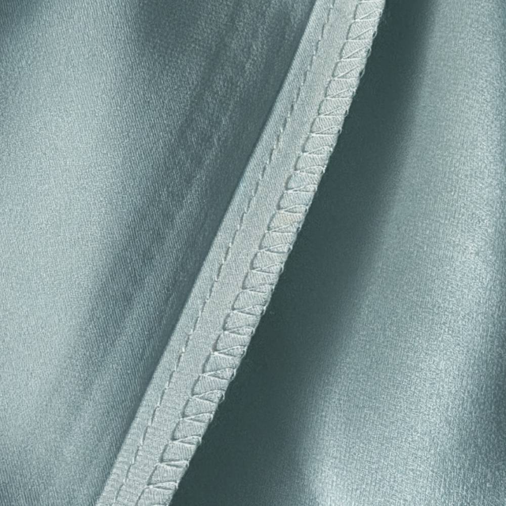 Détail d'une taie en soie vert sauge avec une couture délicate et un aspect lisse et brillant