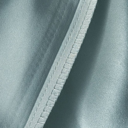 Détail d'une taie en soie vert sauge avec une couture délicate et un aspect lisse et brillant